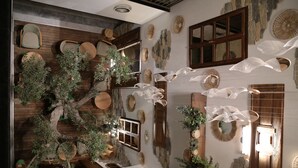 Una habitación con techo de madera, paredes de piedra y varios objetos decorativos, como plantas, muebles de madera y arte mural.