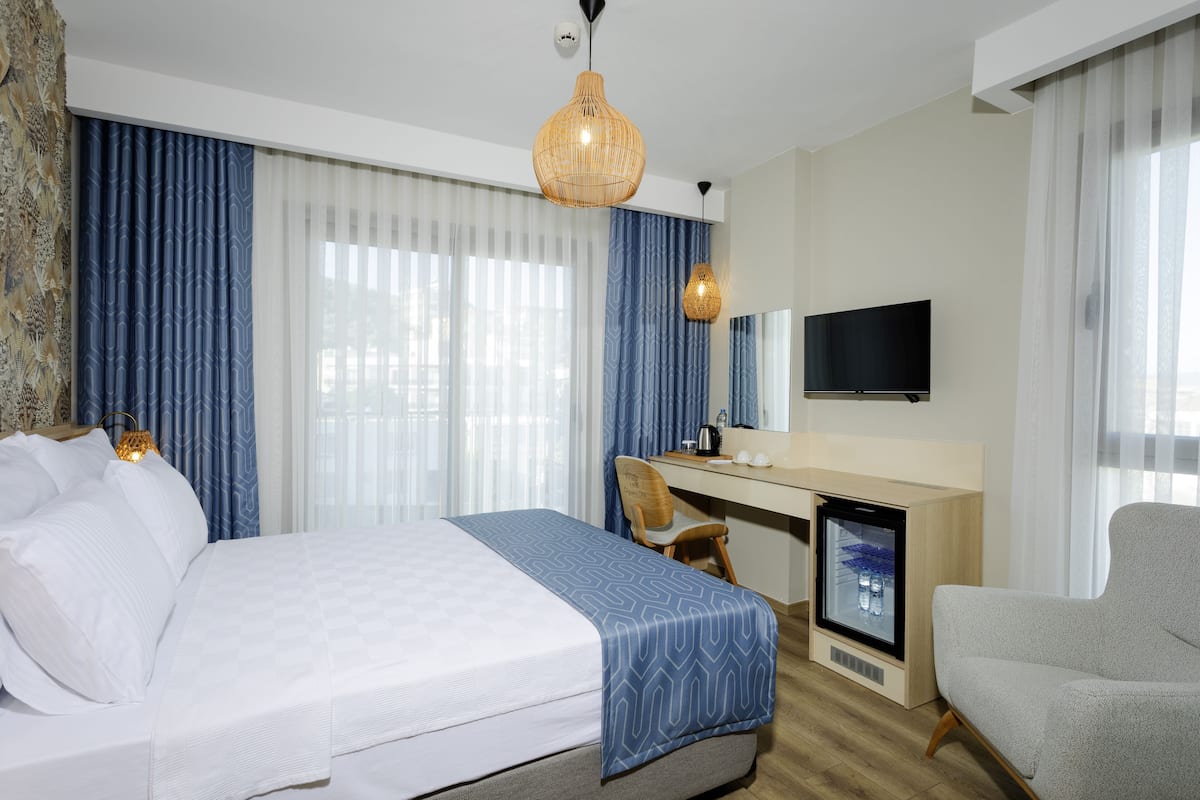 A hotel room with a bed, a desk, a chair, a TV, and a minibar.