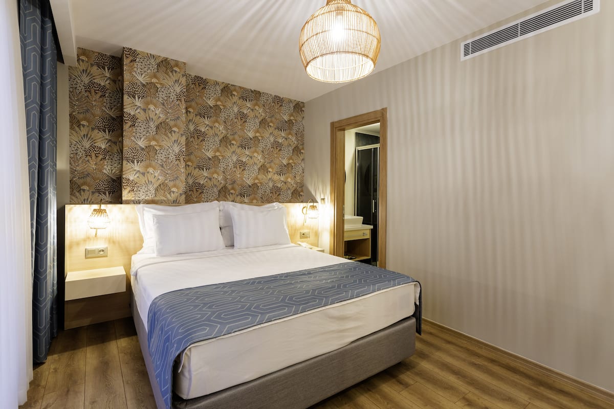 A neatly made bed with a patterned bedspread, bedside lamps, and a wall with a decorative pattern.