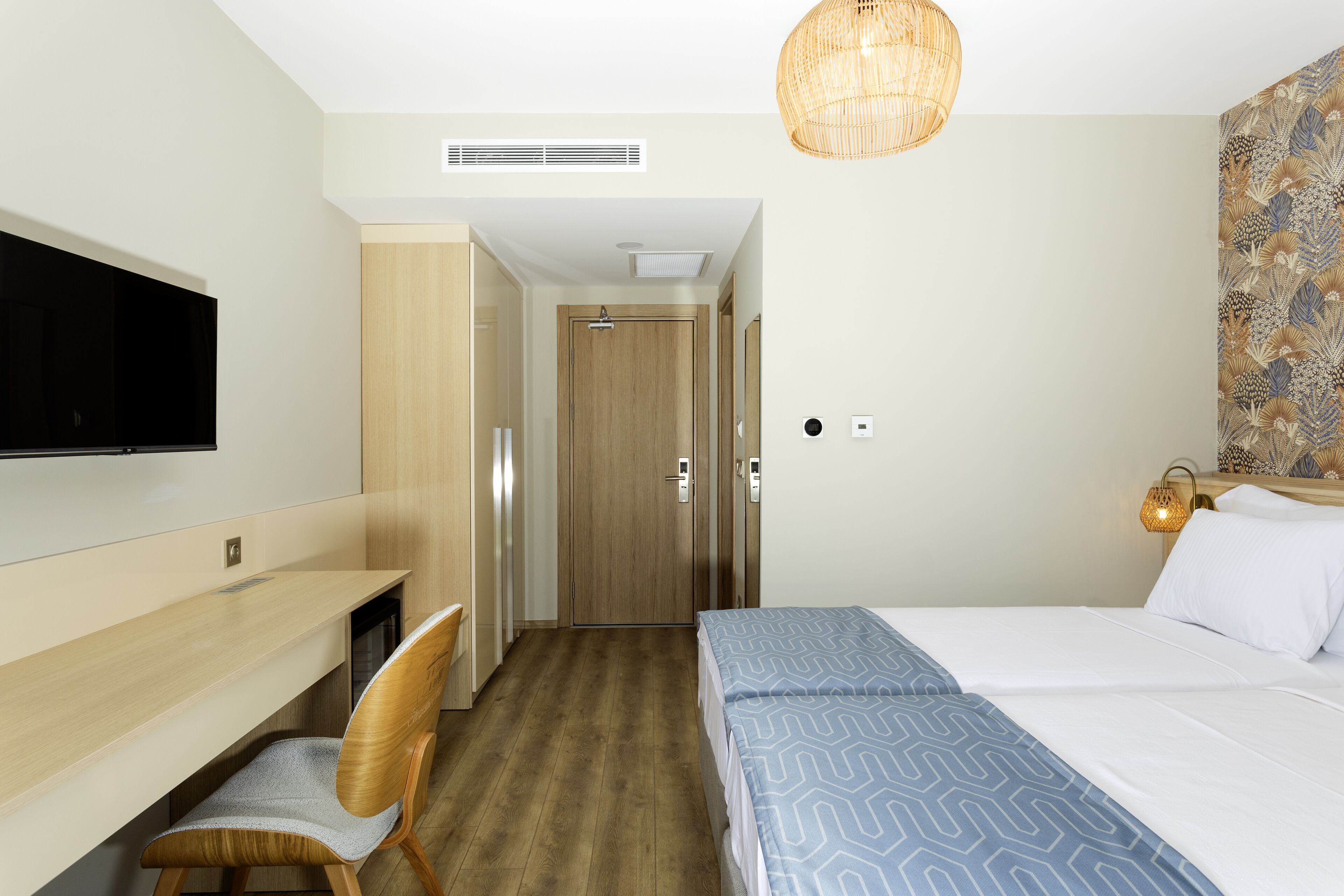A hotel room with a bed, a desk, a chair, a television, and a door leading to another room.