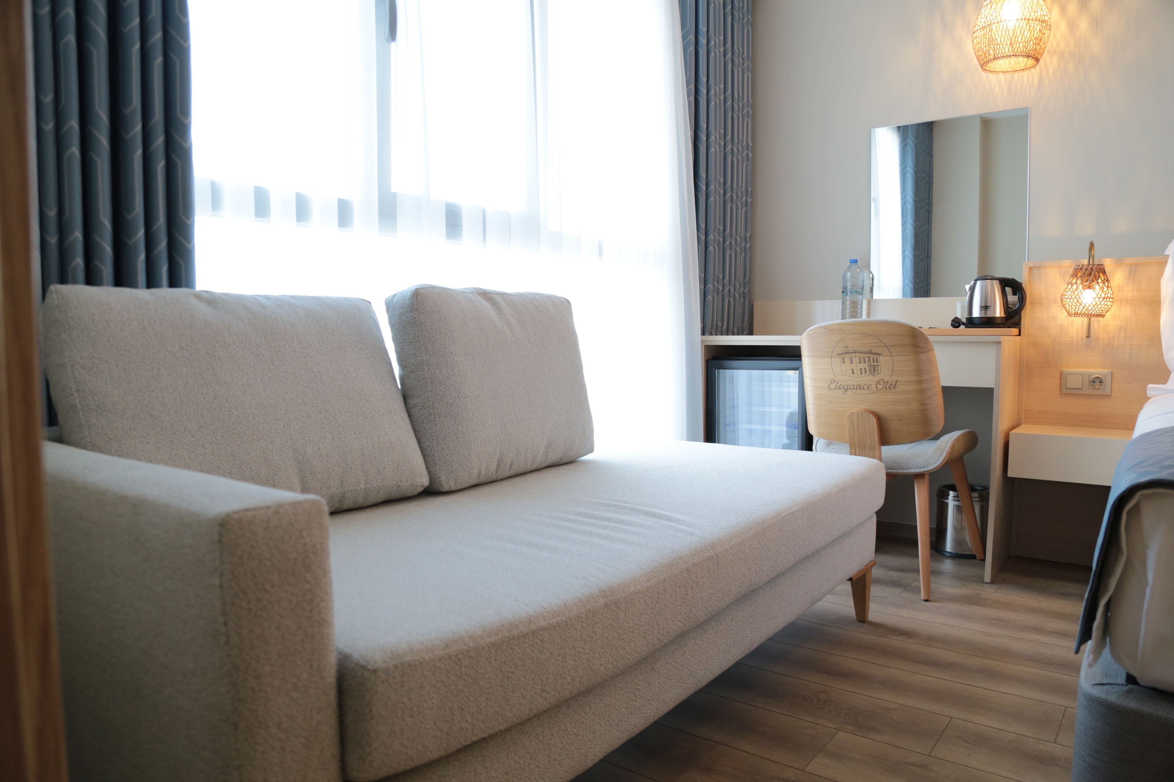 Quarto de hotel moderno com sofá bege, escrivaninha de madeira, cadeira e uma cama.