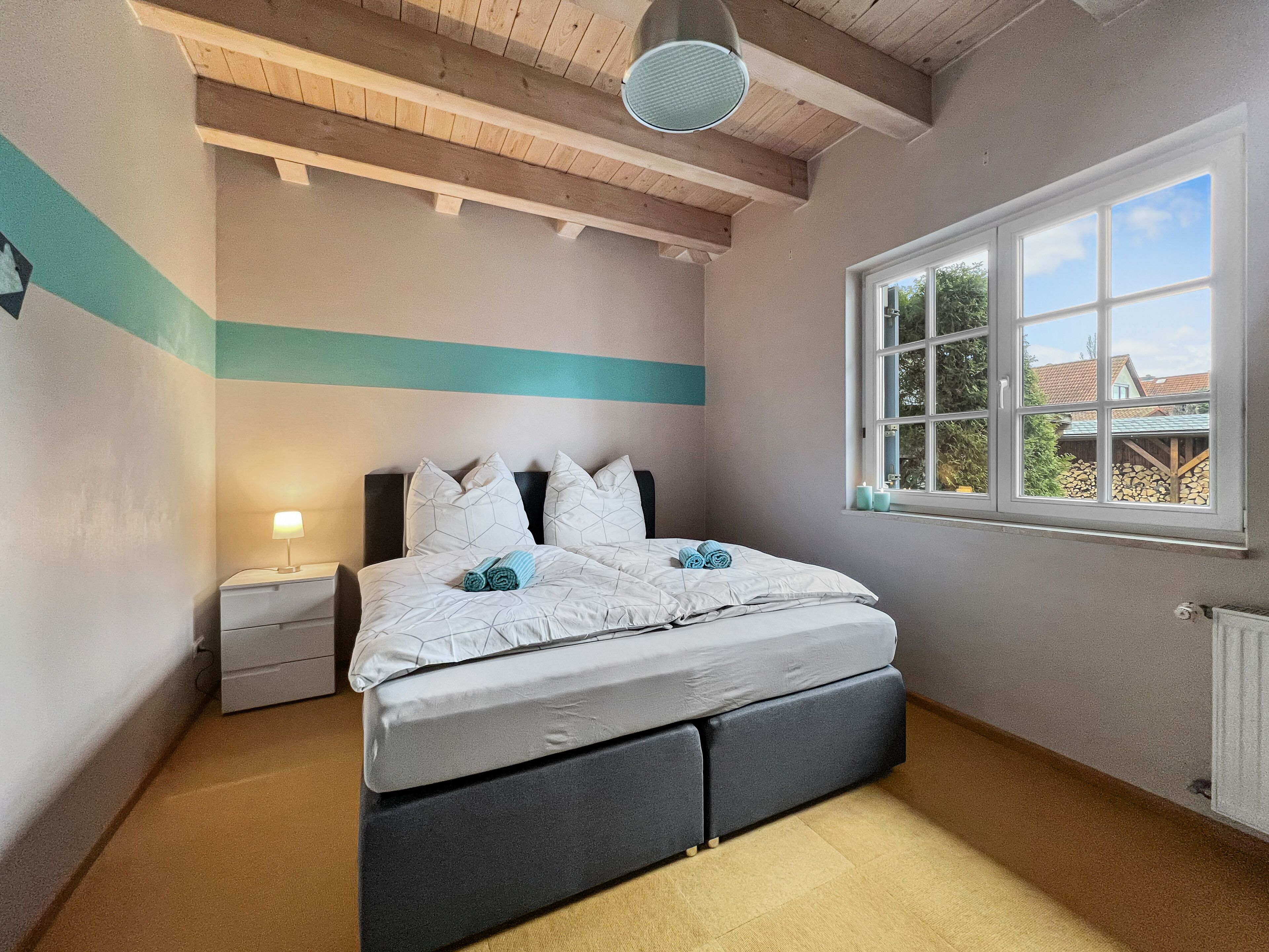 A bedroom with a bed, a nightstand, a lamp, a window with a view, and a ceiling fan.