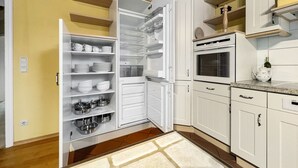 A kitchen with white cabinets, a built-in oven, and a refrigerator with open shelves. - Kamin Indoorschaukel Smart TV Bose Anlage Ferienhaus Kupferschmiede (Wernigerode)