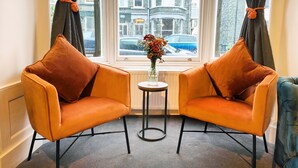 Une pièce avec deux fauteuils orange placés face à une fenêtre donnant sur un immeuble et une voiture.