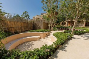 Stroll along the curved pathway to a serene seating area surrounded by lush greenery and a clear sky.