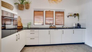 Une cuisine moderne avec des armoires blanches, un comptoir noir, un four encastré et un luminaire suspendu.