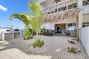 A modern outdoor living area with a thatched roof, a palm tree, and a seating area with cushions.
