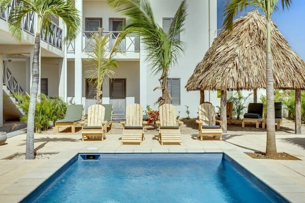 A pool area with lounge chairs and a thatched roof structure.