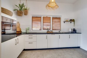 Una cocina moderna con armarios blancos, encimera negra, horno empotrado y lámpara colgante.