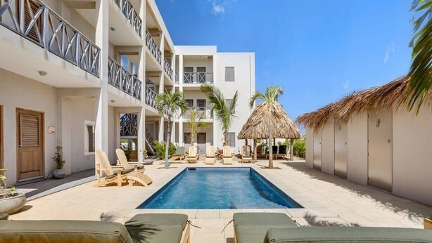 Une cour d’hôtel avec une piscine, des chaises longues et une structure dotée d’un toit de chaume.