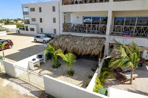 Un edificio moderno con estructura de techo de paja, un espacio de estar al aire libre cubierto y un estacionamiento con coches.