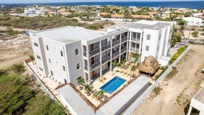 Un hôtel à plusieurs étages doté d’une piscine sur le toit, entouré de verdure et offrant une vue sur la mer.