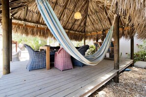 Relax in a serene outdoor space with a thatched roof, wicker chairs, and a hammock.
