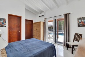 Un dormitorio con una cama, una silla, una mesa y un ventanal corredizo que da a un espacio exterior.