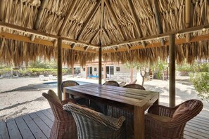 A covered outdoor seating area with a wooden table and wicker chairs, overlooking a pool and lounge chairs. - Salinja Breeze (Kralendijk)