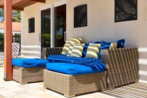 A wicker sofa with blue cushions, a glass door, and decorative wall panels. - Salinja Breeze (Kralendijk)