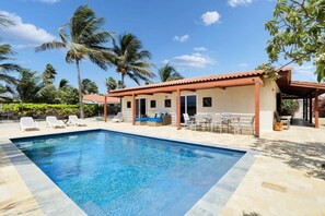 A swimming pool with lounge chairs and a covered seating area, surrounded by palm trees. - Salinja Breeze (Kralendijk)