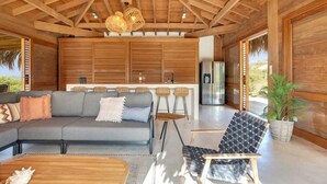 A modern interior with a wooden ceiling, a grey sofa, a black and white patterned chair, and a kitchen area with bar stools. - Kas Berde with a large private pool and spectacular view towards Klein Bonaire (Kralendijk)