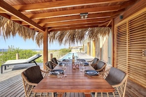 A wooden deck with a table set for dining, overlooking a pool and a scenic view. - Kas Berde with lap pool and sea views (Kralendijk)