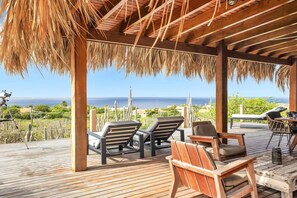 A wooden deck with lounge chairs and a table, overlooking a coastal landscape.