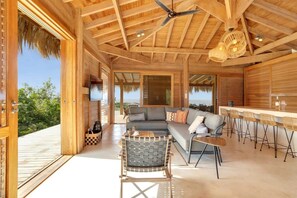 A spacious living area with a wooden ceiling, a sofa set, a dining table with chairs, and a bar area.