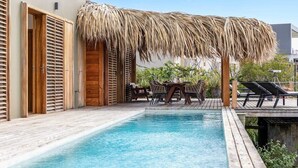 A pool area with a wooden deck, a thatched roof structure, and lounge chairs. - Kas Berde with a large private pool and spectacular view towards Klein Bonaire (Kralendijk)