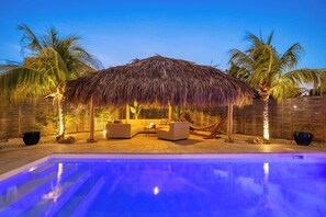 Un espace aménagé au bord de la piscine, avec un parasol en chaume, deux canapés et un hamac.