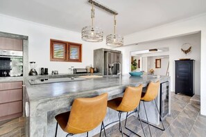 Une cuisine moderne dotée d’un grand îlot central, de tabourets de bar et de luminaires suspendus.