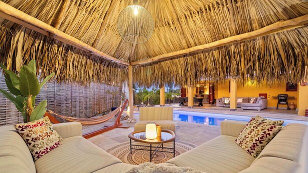 A poolside lounge with a thatched roof, a pool, and a seating area with a table and chairs. - Kas Pura Vida with a very cozy poolside palapa (Kralendijk)