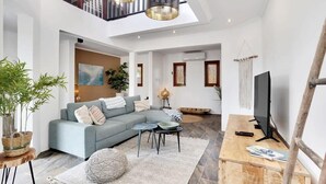 A spacious living area with a sectional sofa, a coffee table, and a TV. There is a staircase leading to an upper level, and a large window providing natural light. - Kas Pura Vida with a very cozy poolside palapa (Kralendijk)