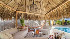 A thatched-roof outdoor seating area with a pool. - Kas Pura Vida with a very cozy poolside palapa (Kralendijk)