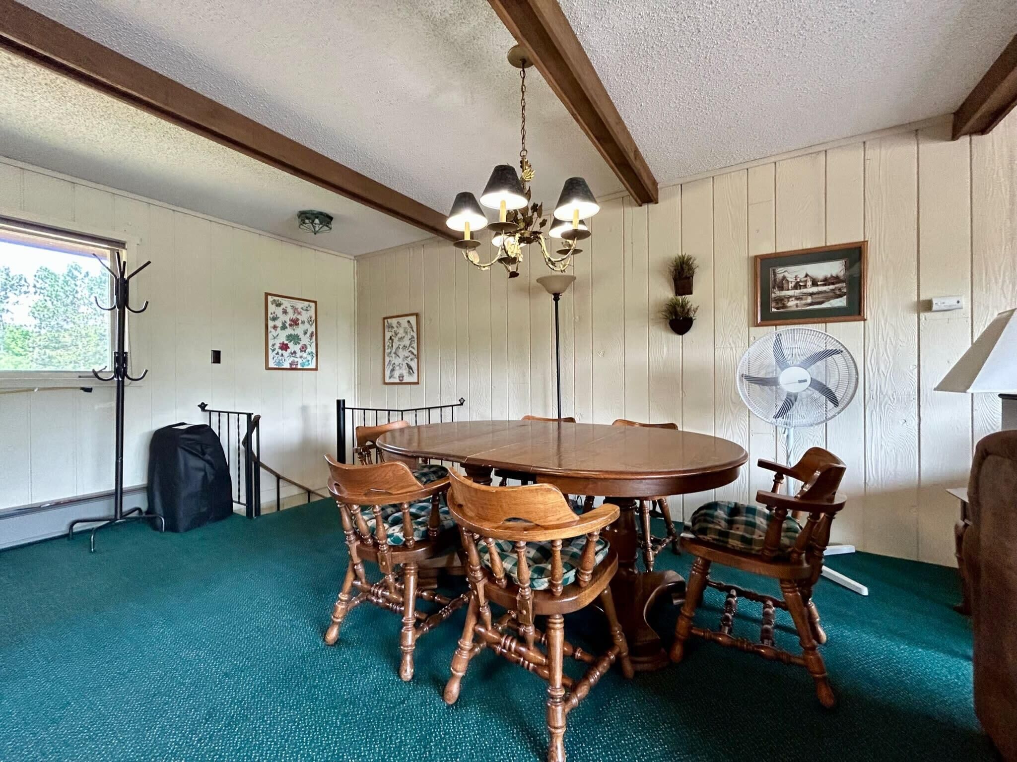 A dining area with a wooden table and chairs, a chandelier, a fan, and framed pictures on the walls.