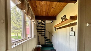 Un pasillo estrecho con techo de madera, una escalera y una ventana con vistas a árboles.
