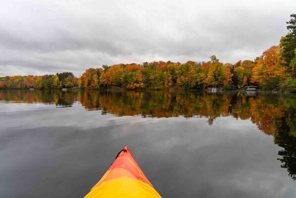 A calm lake with autumn foliage and a kayak in the foreground.