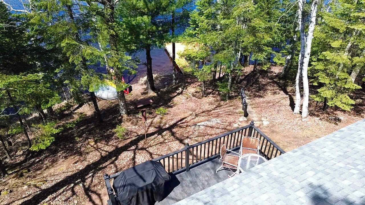 Eine Terrasse mit Grill und überdachtem Tisch, mit Blick auf eine bewaldete Landschaft mit einem See.