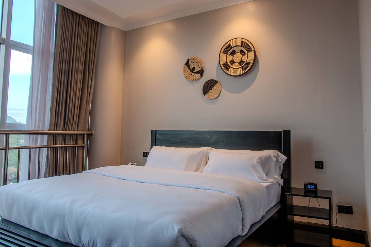 A neatly made bed with white linens, a dark headboard, and a bedside table with a digital clock.