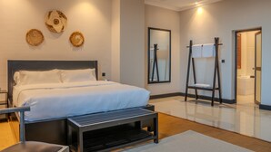 A modern hotel room with a large bed, a bench, a mirror, and a bathroom visible through an open door. - Sanna Boutique Hotel (Arusha)