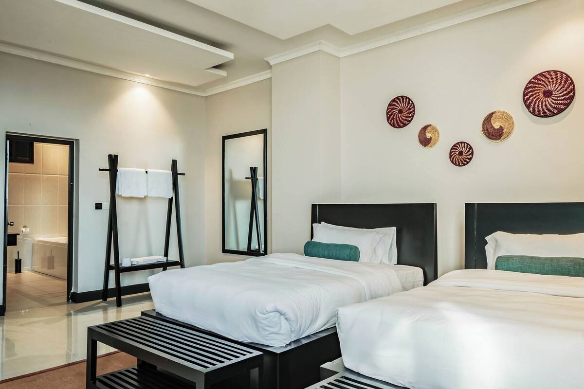 A hotel room with two beds, a bathroom, and a hallway.