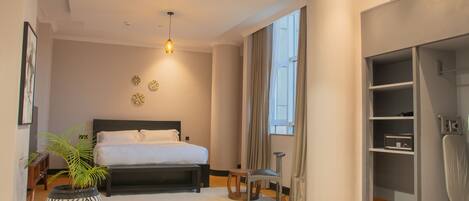 A modern bedroom with a large bed, a potted plant, a chair, and a walk-in closet.