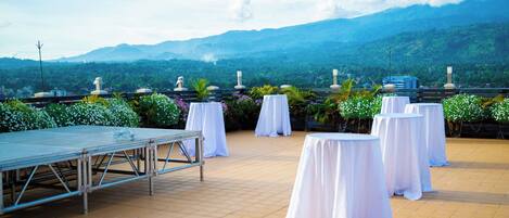 A terrace with white tablecloths and a stage, overlooking a mountainous landscape.
