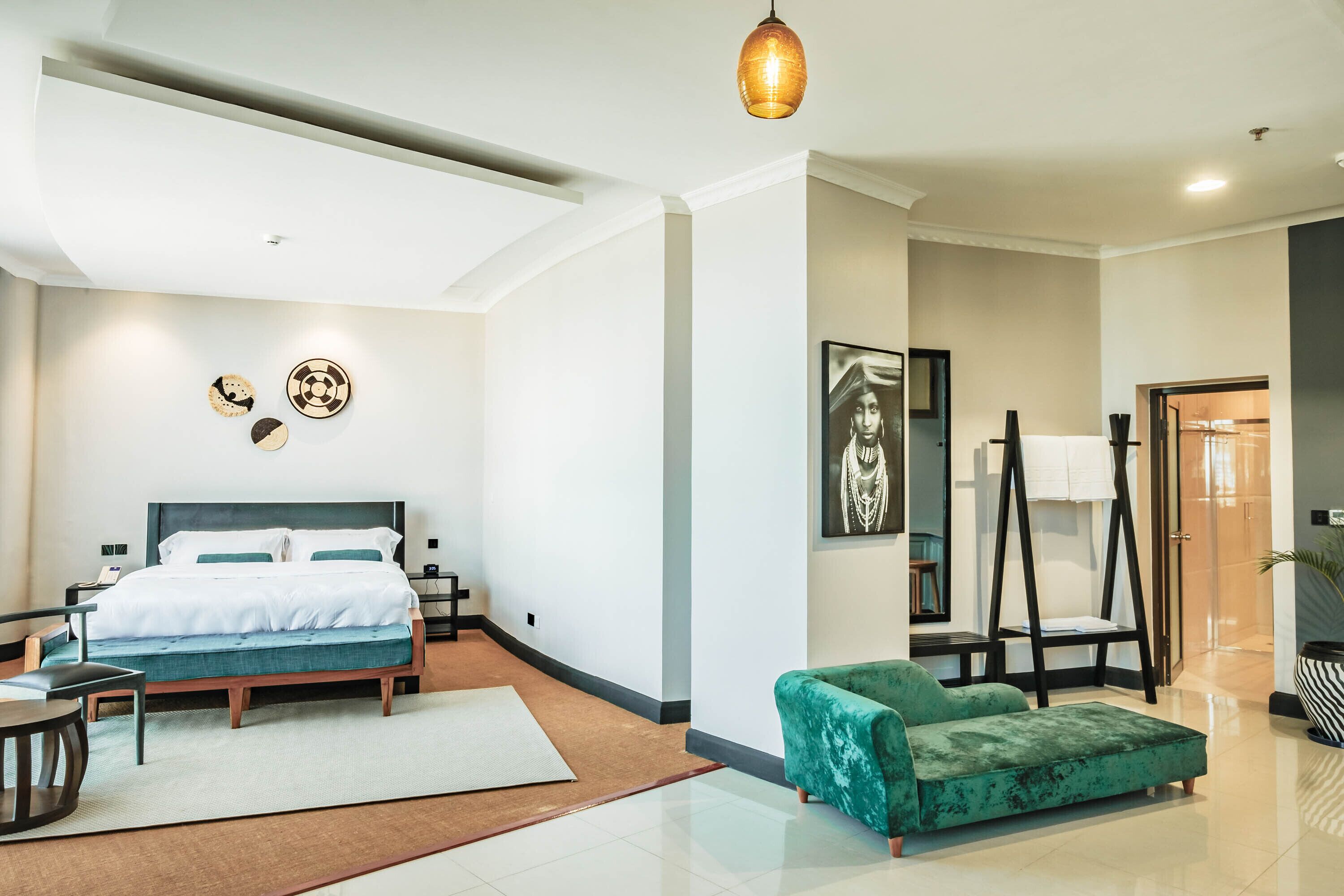 A modern hotel room with a bed, a green sofa, a desk, and a painting on the wall.