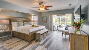 A bedroom with a bed, bedside tables, a bench, a ceiling fan, and a view of the outdoors. - Gorgeous Punta Gorda Home w/ Lanai & Private Pool! (Punta Gorda)
