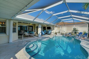 An indoor swimming pool with a glass ceiling, lounge chairs, and a patio area.