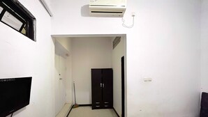 A narrow hallway with a door at the end, a black cabinet, and an air conditioning unit mounted on the wall. - Hotel O Guest House Sae Madani (Sepaku)