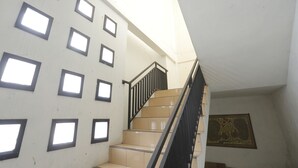 A staircase with a black railing and beige steps, leading to a landing with a patterned wall. - Hotel O Guest House Sae Madani (Sepaku)