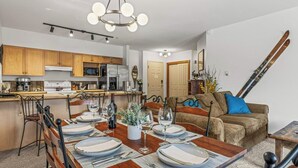 Une cuisine moderne avec des meubles en bois, une table à manger pour six personnes et un coin salon avec un canapé et un porte-skis.