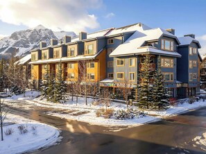 A multi-story hotel with a snow-covered roof, a mountain backdrop, and a clear sky.