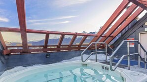 Un bain à remous avec vue sur les montagnes, une terrasse en bois et un escalier en métal.