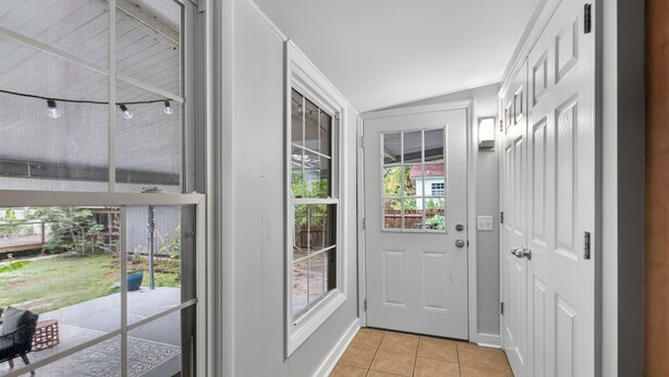 A hallway with a door leading to a backyard, a window with a view of the outdoors, and a tiled floor.