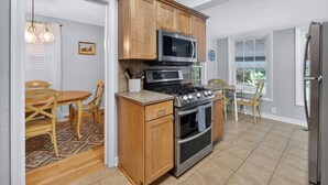 A kitchen with wooden cabinets, a stove, oven, microwave, and a dining area with chairs and a table.